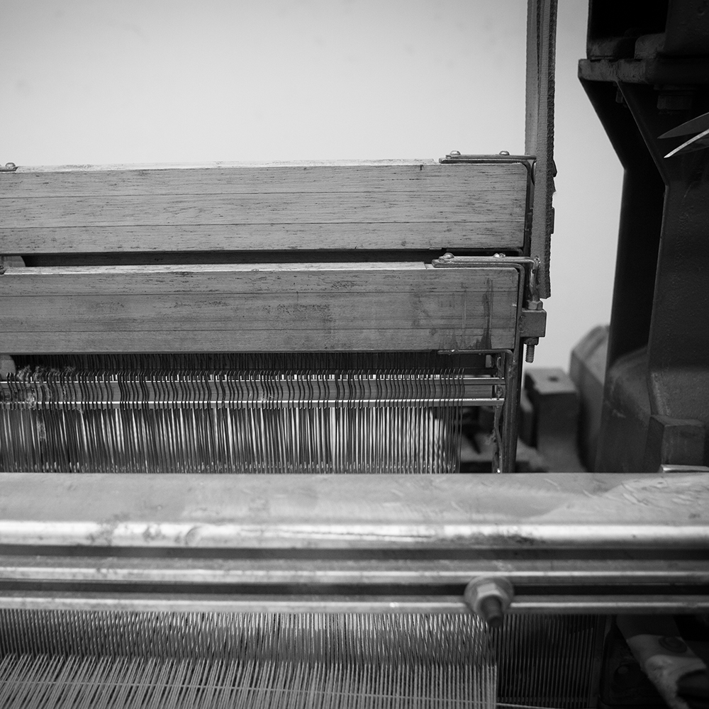 black and white photograph front of Draper power shuttle loom producing selvedge textiles