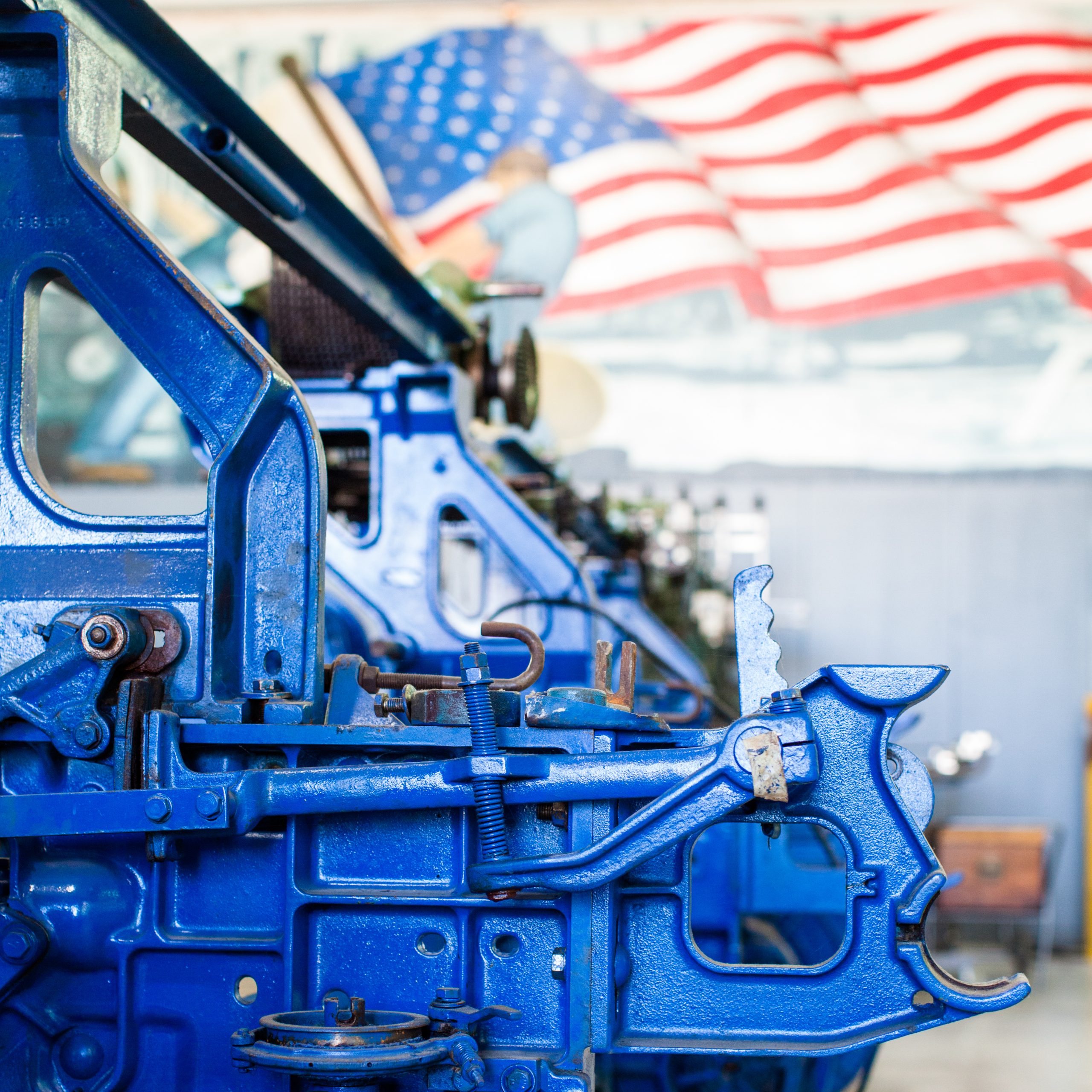 color photograph with blue toyoda industrial loom in foreground with American flag mural in background